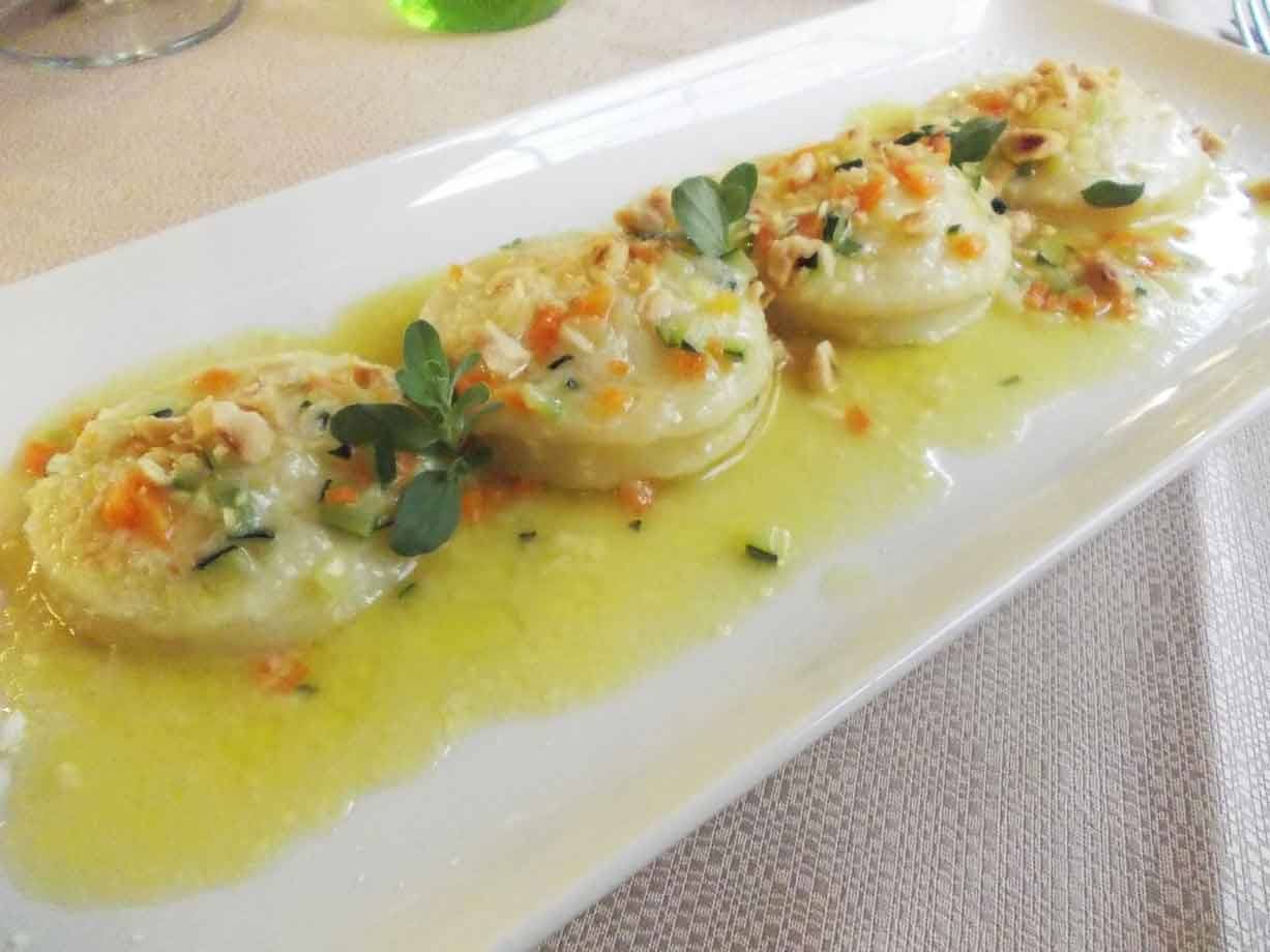 Quattro ravioli al burro salvia con noci e verdure, serviti su piatto bianco