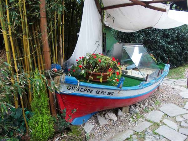Red and blue wooden boat named Giuseppe displayed among bamboo, flowers on deck