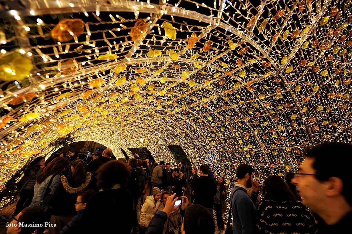 Tunnel di luminari dorate, folloia di persone passeggia e fotografa sotto le luci