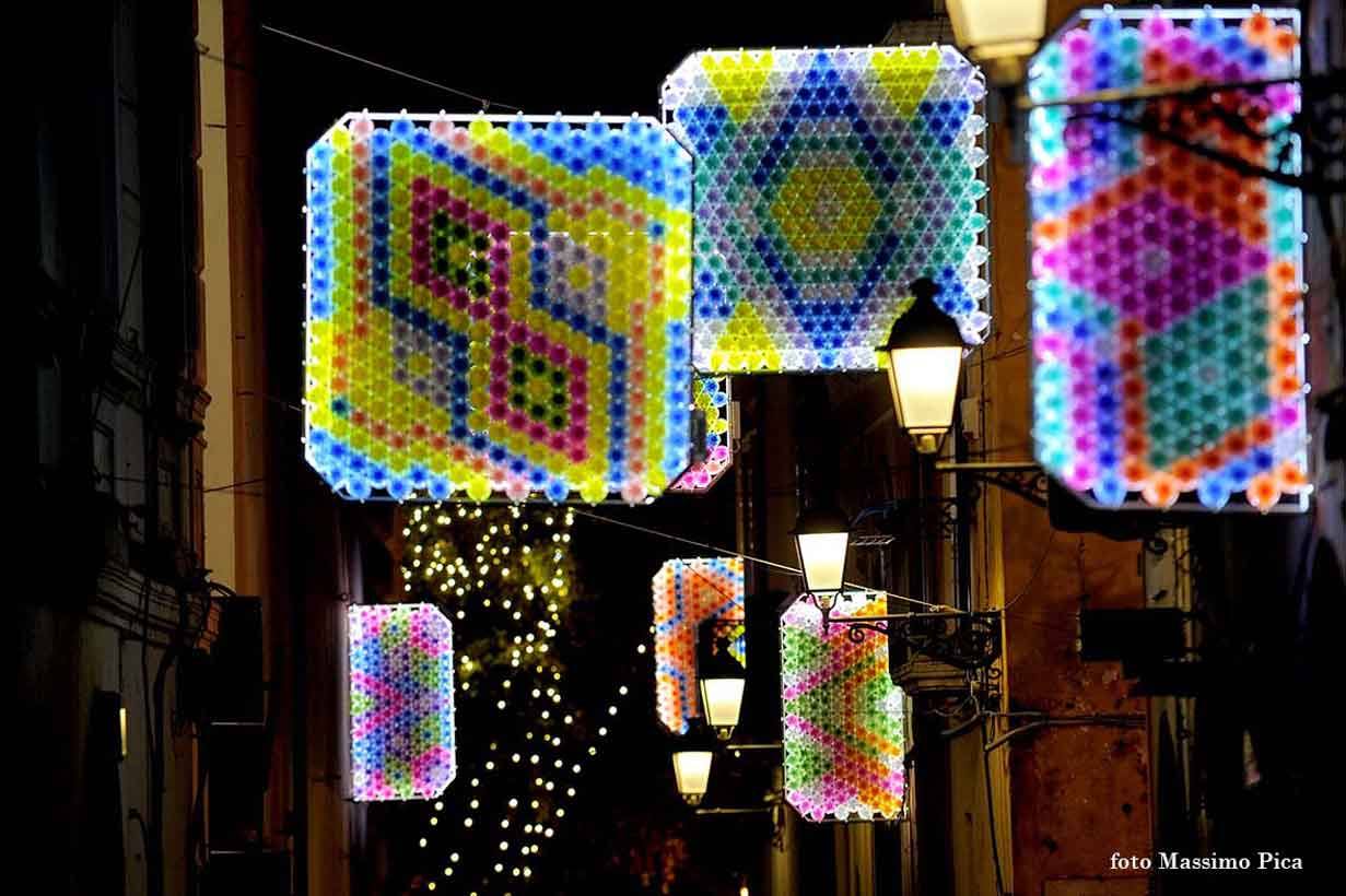 Luminarie colorate appese sopra un vicolo notturno tra lampioni accesi