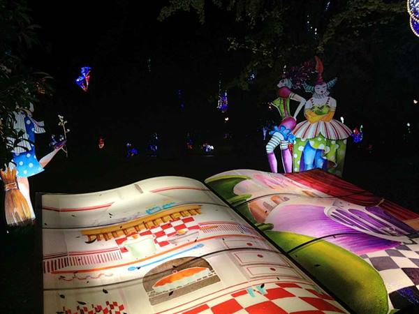 Glowing lantern sculptures of colorful characters beside a giant illuminated book