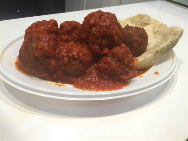 Meatballs in tomato sauce with bread on paper plate, indoor light