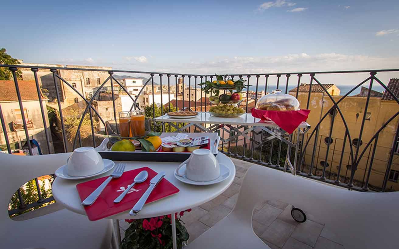 Colazione su terrazza con tavolo bianco, tazze e frutta davanti ai tetti