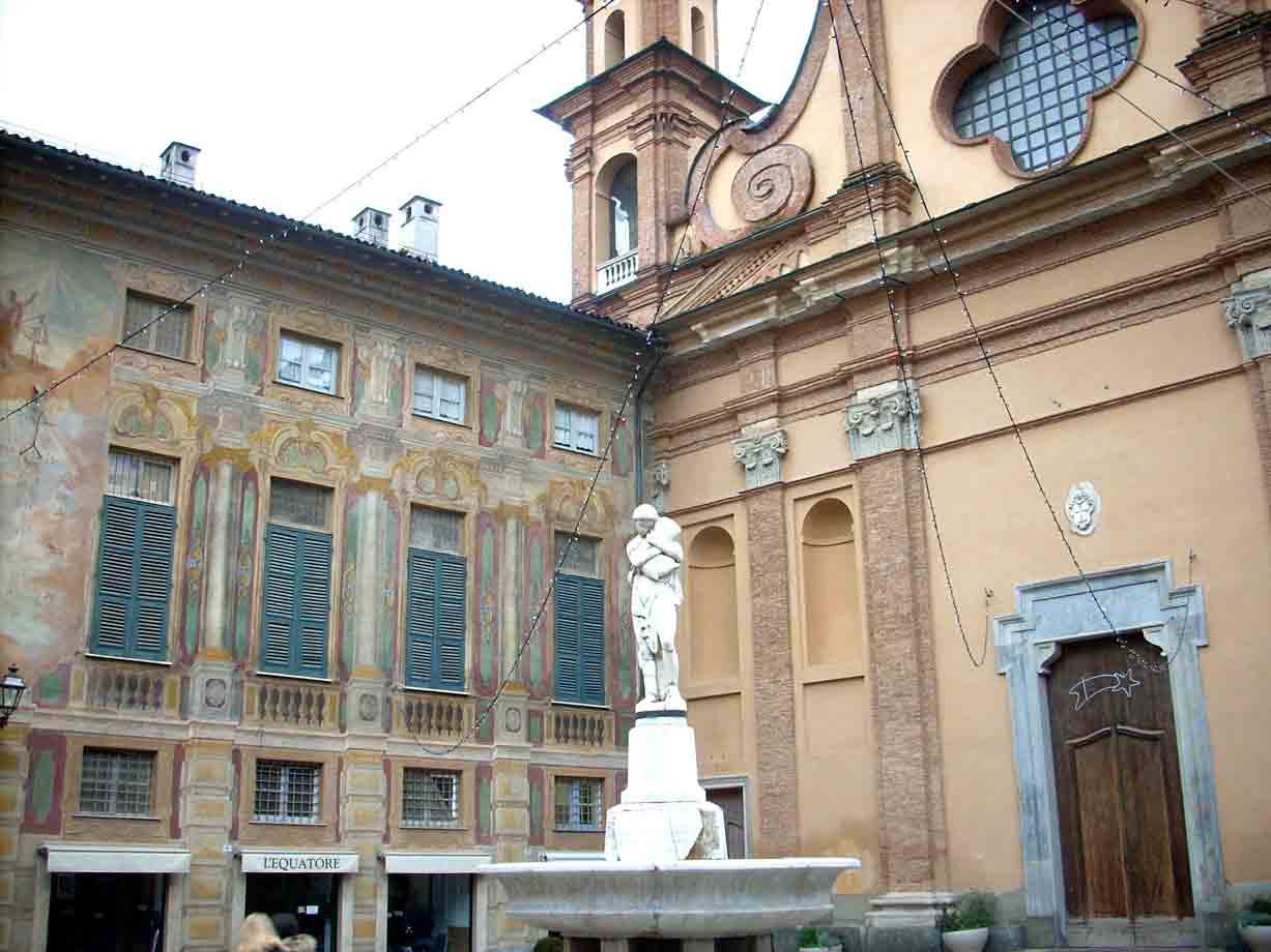 Statua su fontana davanti a chiesa barocca e palazzo affrescado con persiane verdi