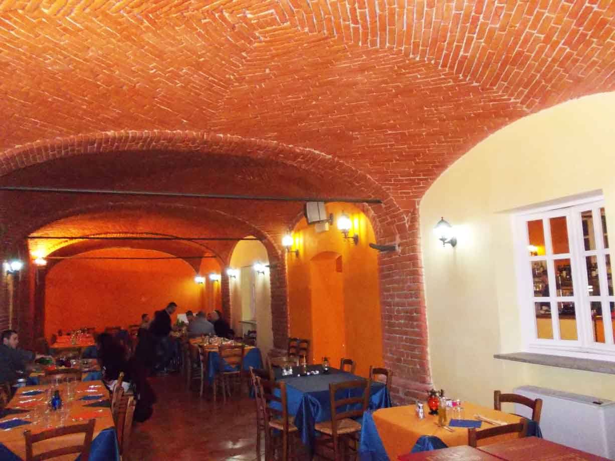 Sala di ristorante con volte in mattoni rossi, tavoli apparecchiati e ospiti
