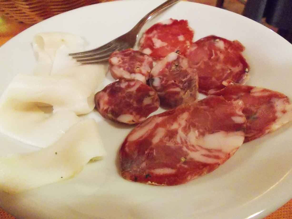 Fette di salame e formaggio bianco su piatto di ceramica, forchetta in metallo