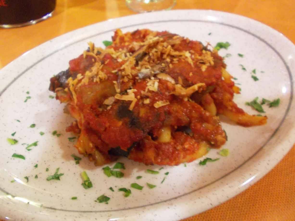 Piatto di pasta al forno con pomodoro e cipolla fritta, su tovaglia arancione