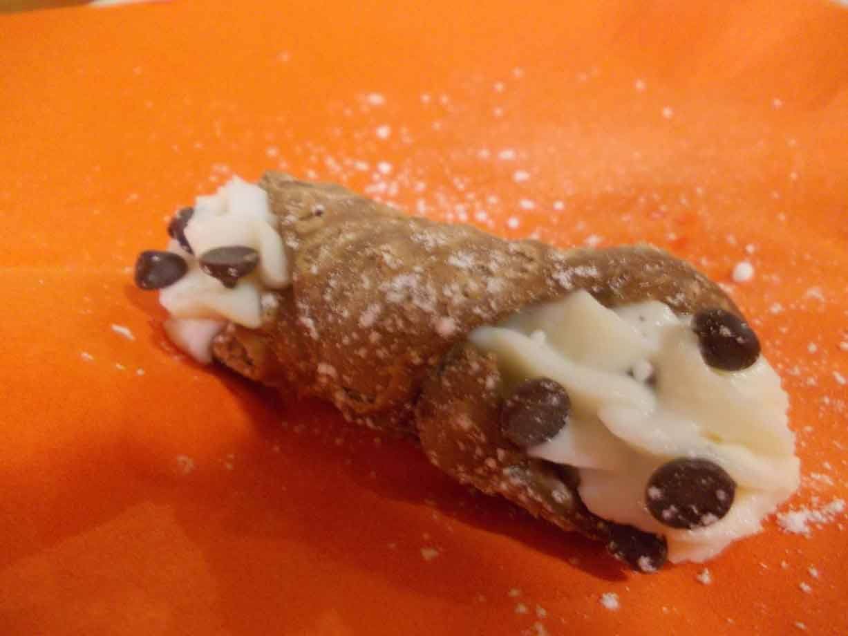 Cannolo siciliano con ricotta e gocce di cioccolato su carta arancione