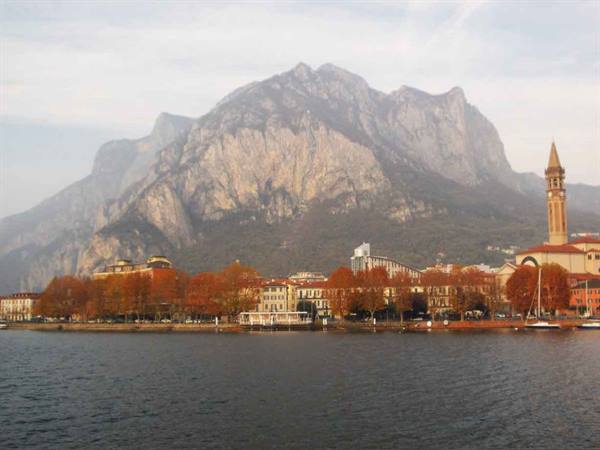 Lecco lakeside in autumn beneath Resegone mountain, bell tower and red trees