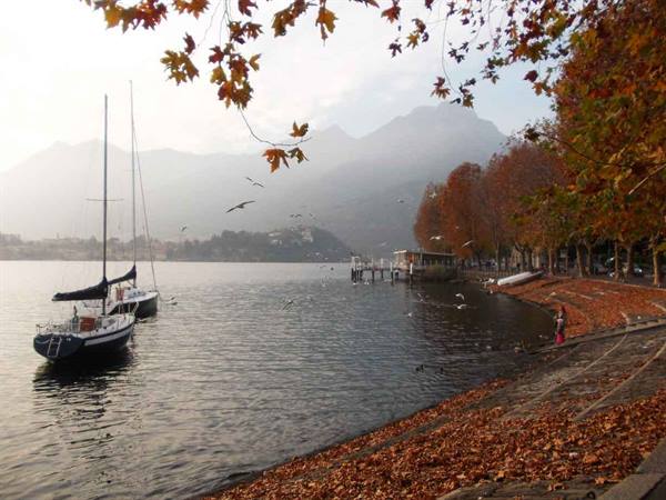 Sailboat moored along Lecco's autumn lakeside promenade, shore covered in leaves