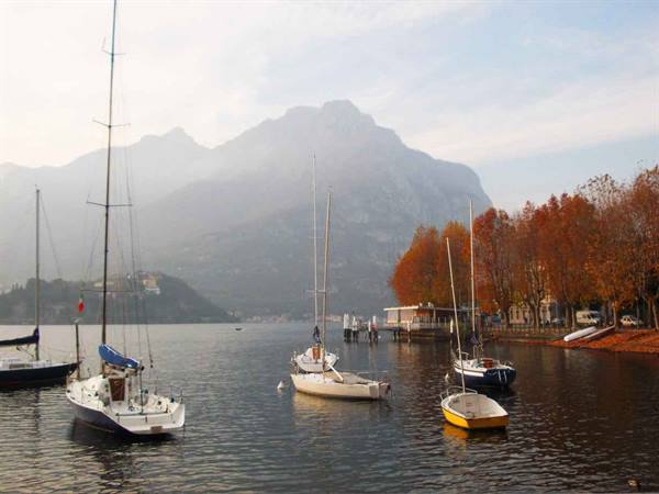 Sailboats moored on Lake Lecco, misty mountains and autumn trees along the shore