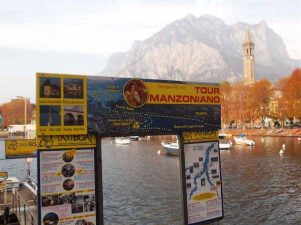 Manzoni tour boards and taxi boat on Lecco lakefront, bell tower and mountain