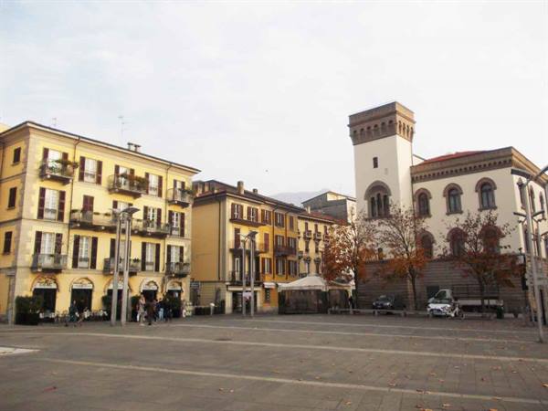 Square with medieval stone tower, yellow buildings with balconies, people walking