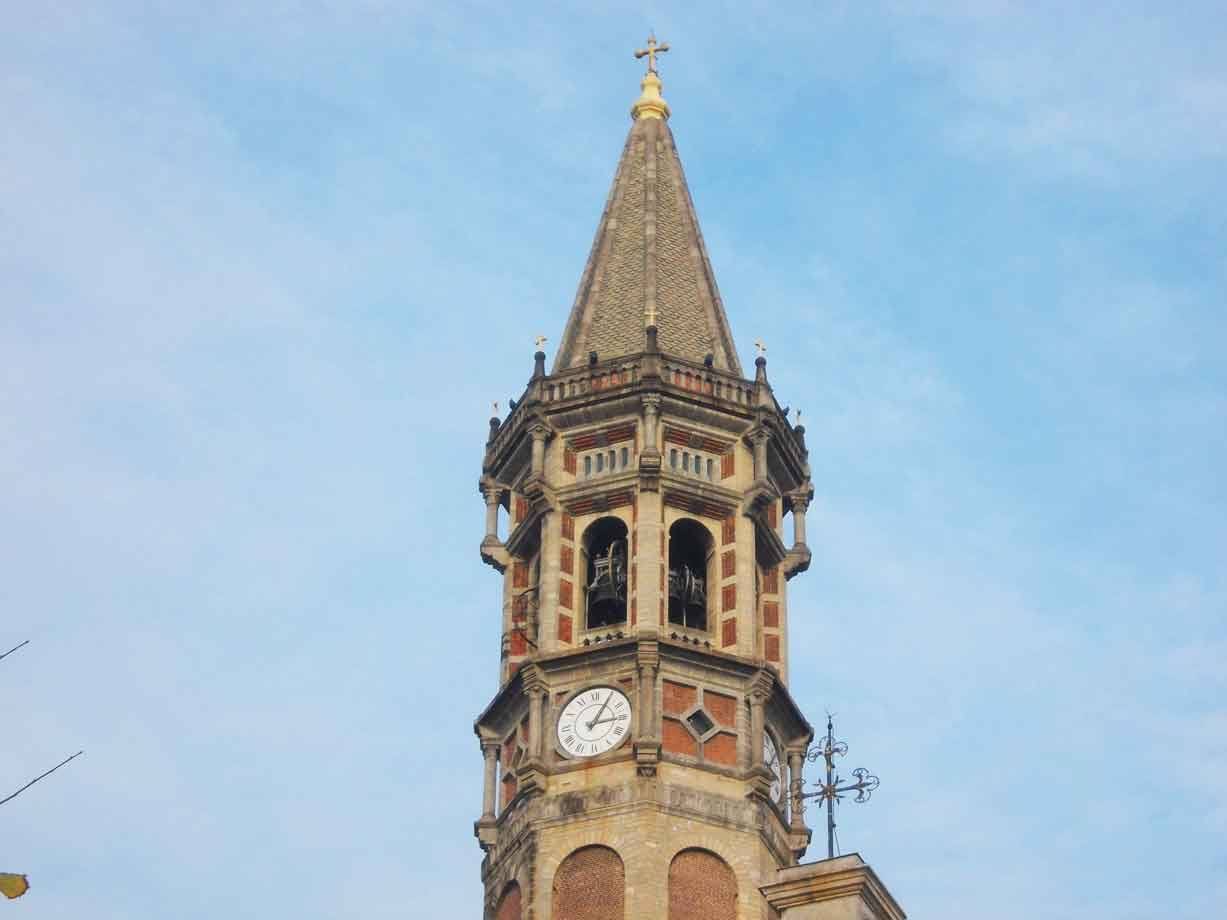 Campanile in mattone e pietra con orologio e guglia conica contro il cielo azzurro