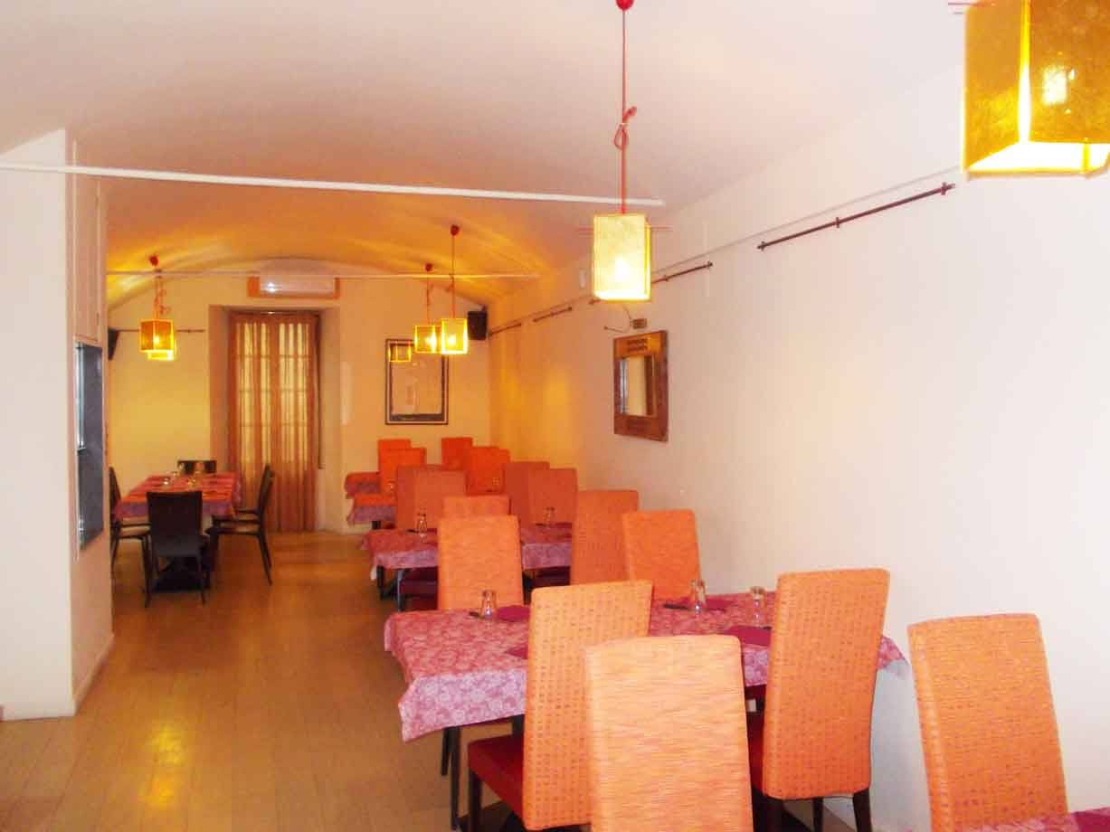 Sala di ristorante con tavoli apparecchiati, sedie arancioni e lampade gialle appese