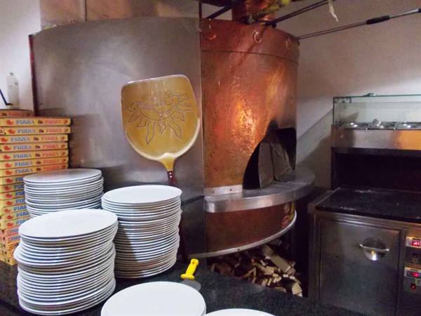 Copper wood-fired pizza oven with decorated peel, stacked plates and boxes