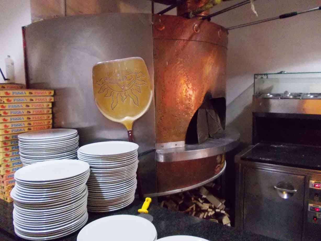 Forno a legna in rame con pala decorata, piatti impilati e scatole di pizza