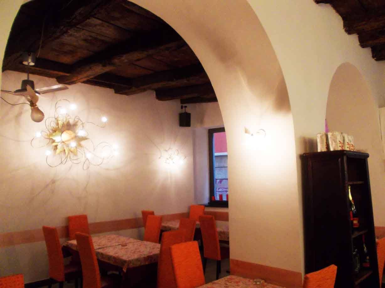 Sala di ristorante con arcate bianche, soffitto a travi in legno e sedie arancioni