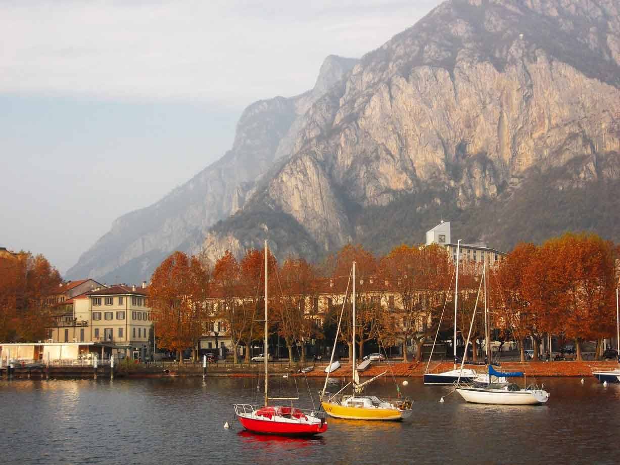 Barche a vela colorate nel porto di Lecco, montagna e alberi autunnali