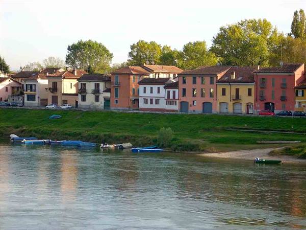 Colorful houses on the grassy Ticino riverbank, rowboats moored on the sand