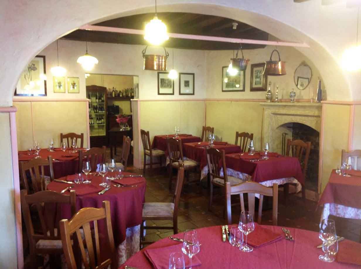 Sala di trattoria con tavoli apparecchiati a tovaglie rosse, camino e rame appeso