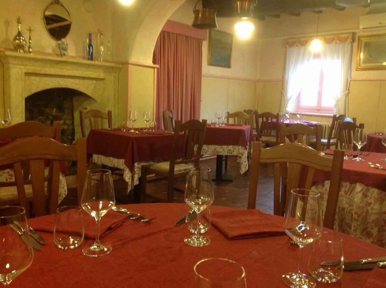 Sala di trattoria con tavoli apparecchiati a tovaglie rosse, caminetto e luce calda