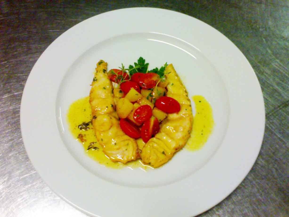 Filetti di pesce con pomodorini e patate su piatto bianco, salsa allo zafferano