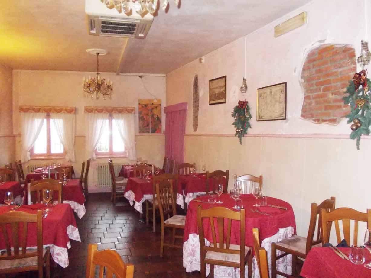 Sala di trattoria con tavoli apparecchiati, tovaglie rosse, sedie di legno e lampadari
