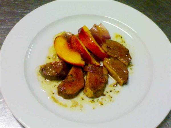 Sautéed meat slices with peaches on a white plate in the kitchen