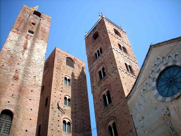 Medieval brick towers of Albenga and cathedral rose window under blue sky