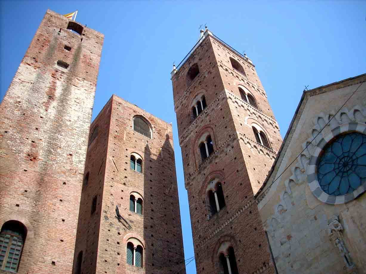 Torri medievali in mattoni di Albenga e rosone della cattedrale sotto cielo azzurro