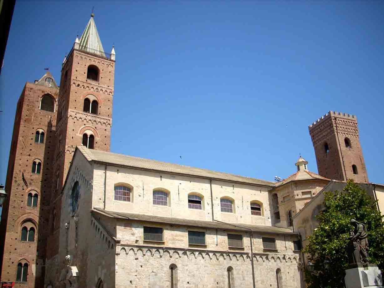 Cattedrale di Albenga: facciata in pietra chiara, campanile e torri in mattoni sotto cielo azzurro