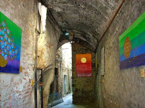 stone-vaulted alley with colorful painted canvases hung on the walls