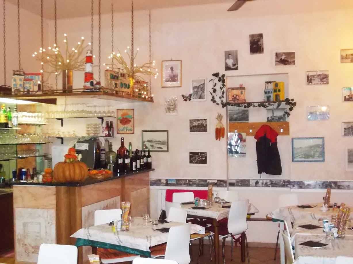 Sala di trattoria con bancone in marmo, bottiglie, zucche, foto d'epoca alle pareti