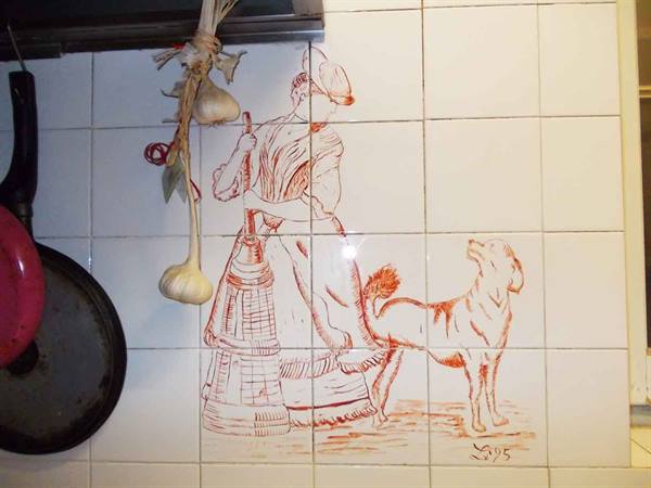 White kitchen tiles with sepia drawing of woman and dog, hanging garlic