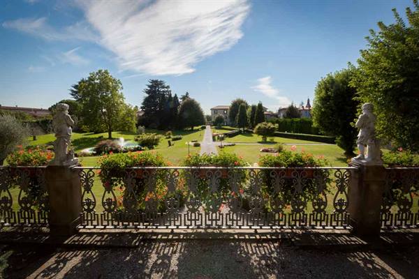 Wrought iron balustrade with statues and flowers above green garden, blue sky