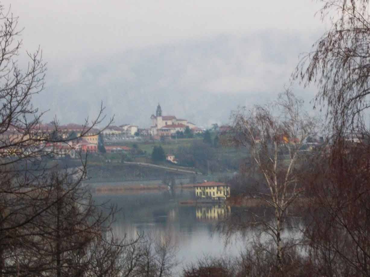 Paese con campanile sul lago, nebbia, rami spogli sul davanti