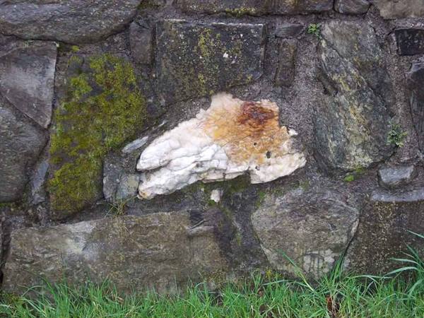 Grey stone wall with green moss and a whitish stone in the center