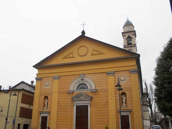Ochre facade of Santi Gervasio e Protasio church with bell tower under gray sky