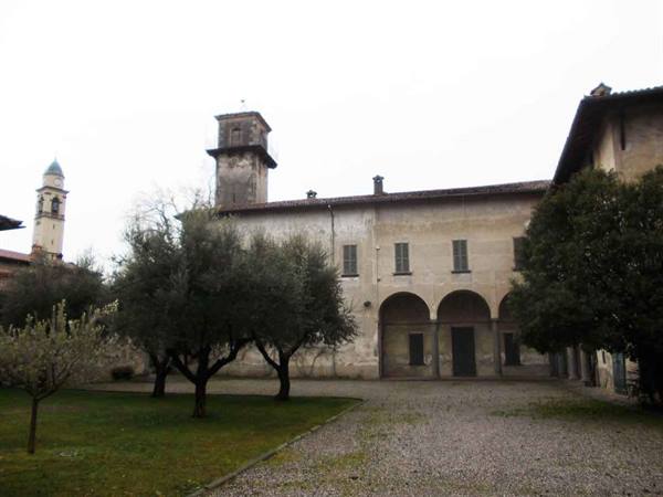 Gravel courtyard with arched portico, trees and old building with tower