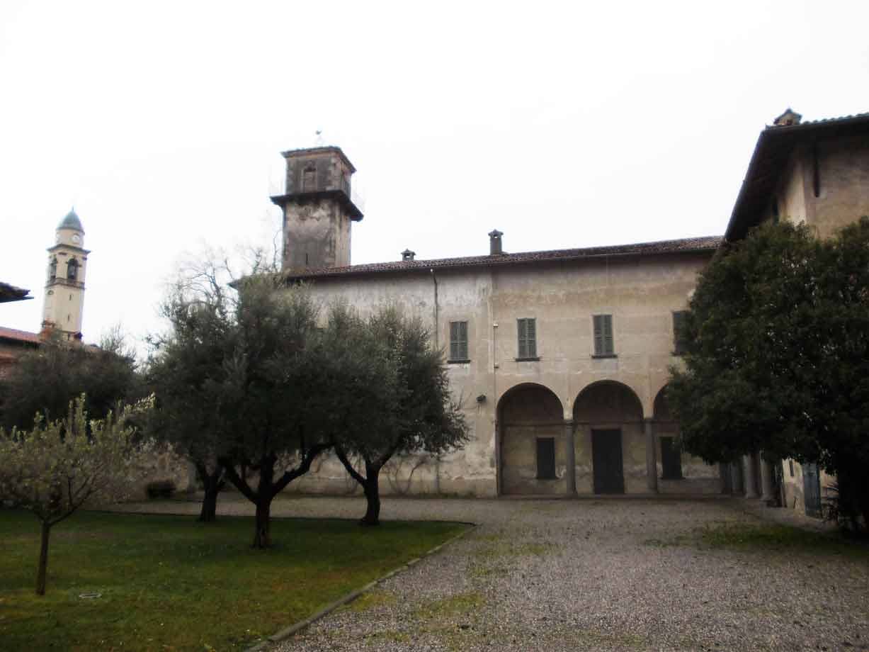 Cortile gravel con portico ad archi, alberi e antico edificio con torre
