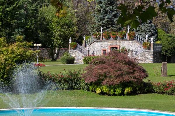 Fountain in foreground and stone staircase with statues among flowered gardens
