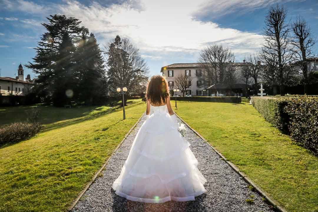 Sposa in abito bianco cammina su vialetto di ghiaia verso villa storica