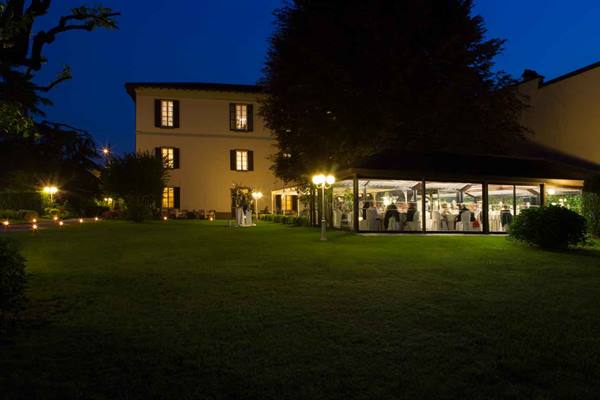 Historic villa at night with lit garden and glass banquet hall