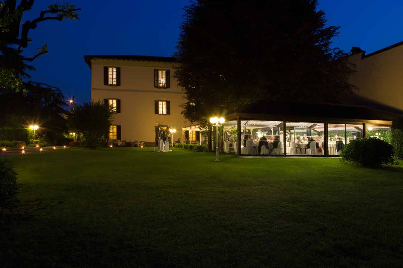 Villa storica di notte con giardino illuminato e sala in vetro per banchetti