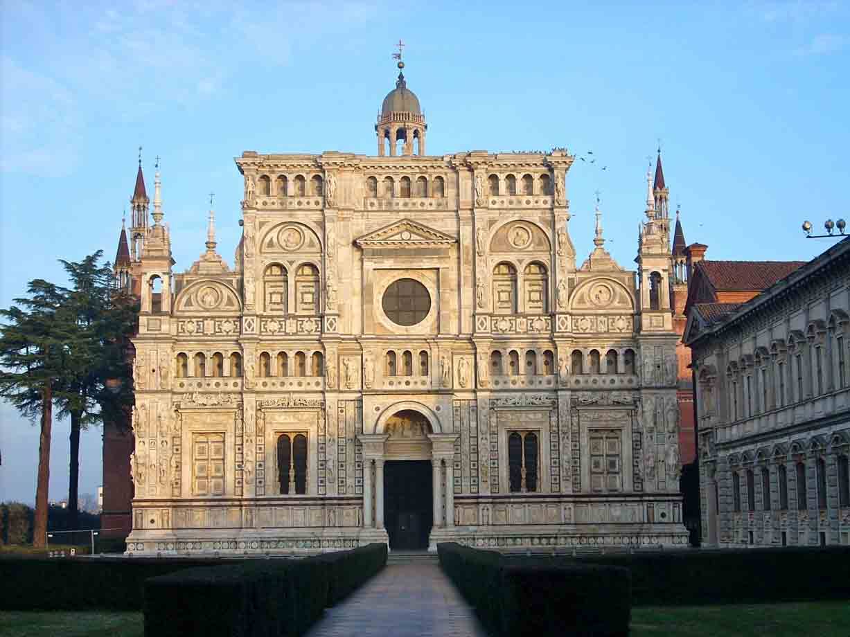 Facciata marmorea della Certosa di Pavia illuminata dal sole, siepi e passeggiata davanti