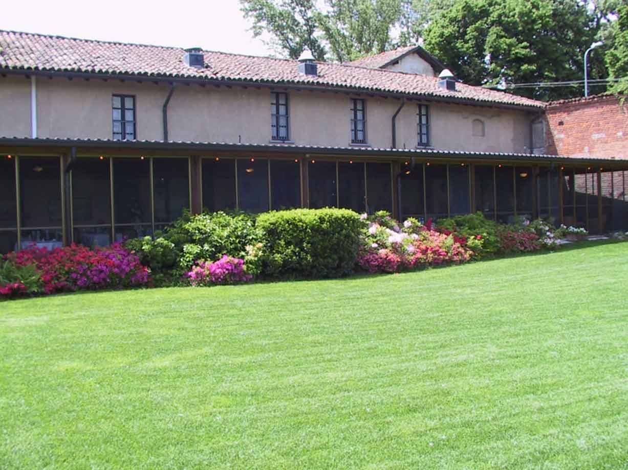 Cascina con tetto di tegole, veranda vetrata e aiuole di azalee sul prato