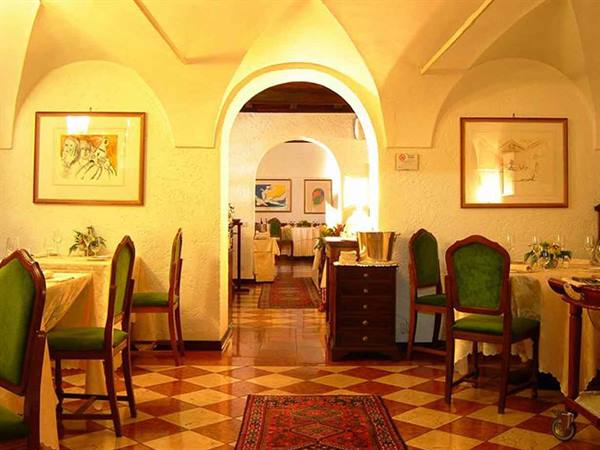 Restaurant dining room with white vaulted ceilings, green chairs, checkered floor and framed paintings