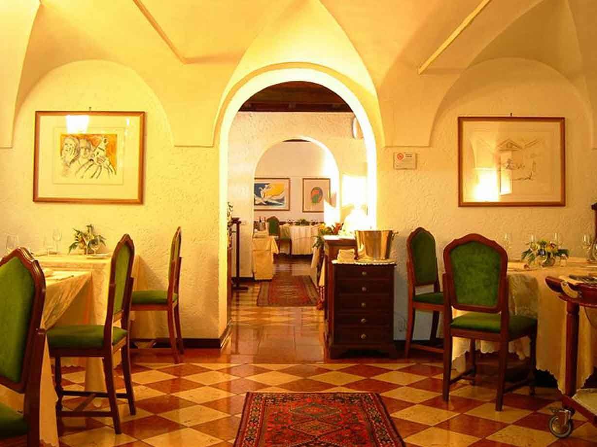 Sala di ristorante con volte bianche, sedie verdi, pavimento a scacchi e quadri incorniciati