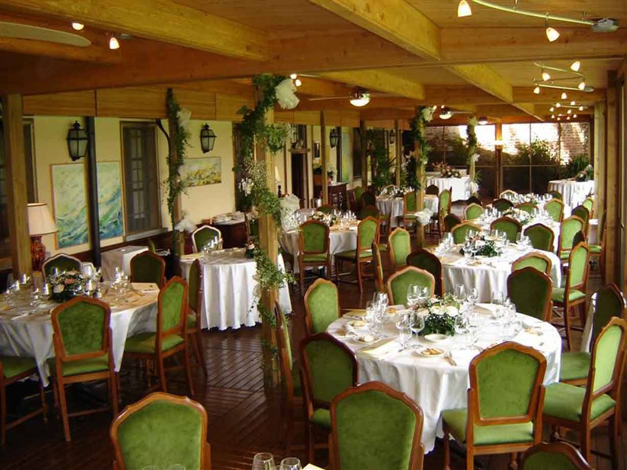 Sala ristorante con tavole apparecchiate, sedie verdi, travi in legno e decorazioni floreali